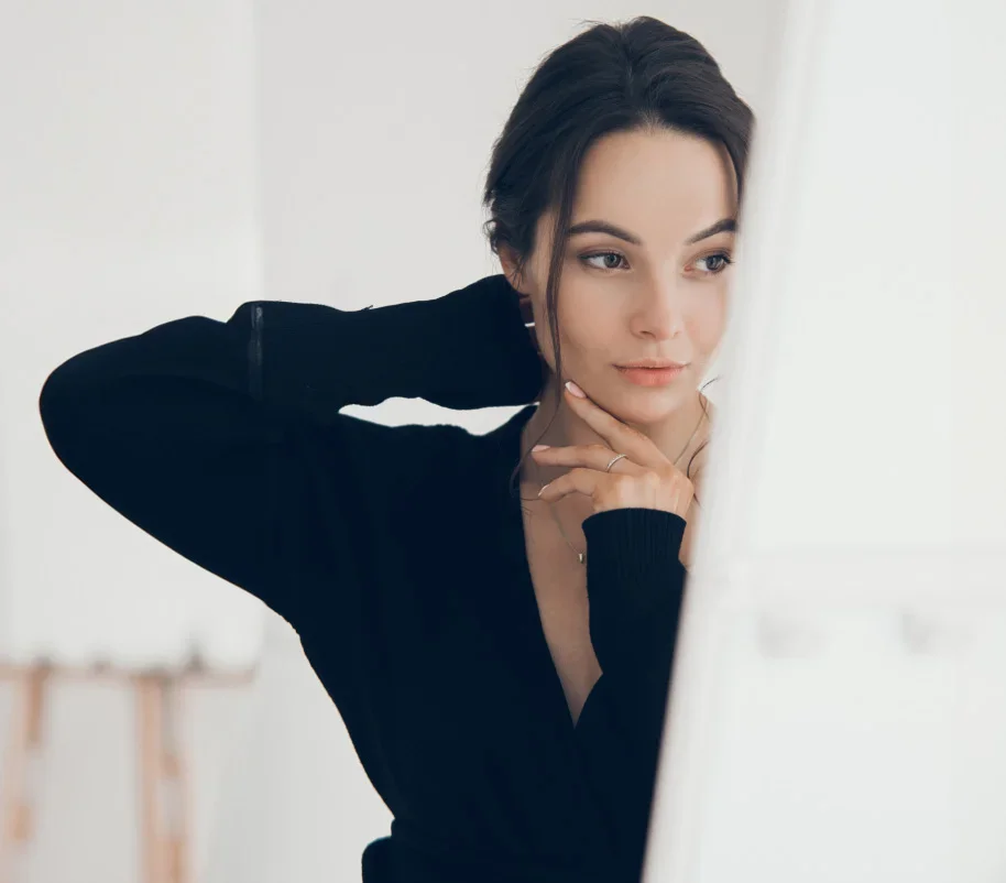 Woman in black turtleneck sweater posing thoughtfully with hand under chin in bright minimalist interior - Fat transfer in Evansville, IN