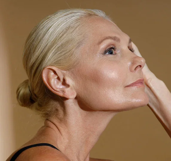 Mature woman with elegant updo hairstyle touching face, showcasing natural aging and skincare - Facelift in Evansville, IN