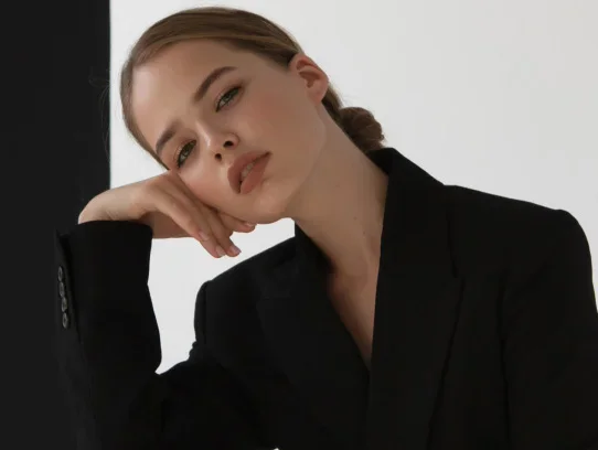 Woman in black blazer resting head on hand with contemplative expression against white background - Injectables in Evansville, IN