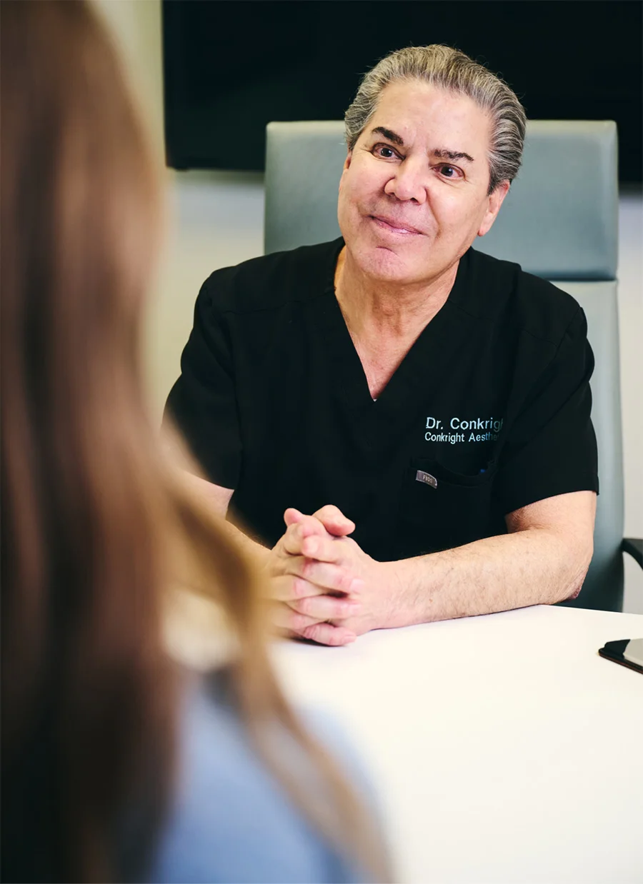 Doctor James Micheal Conkright MD in black scrubs consulting with patient across desk in clinical setting - in Evansville, IN