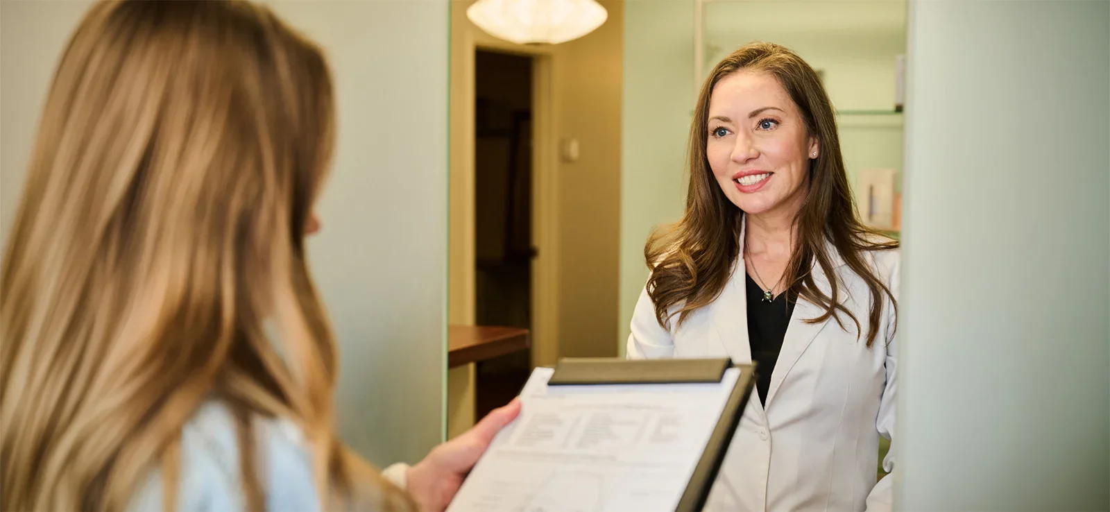 Woman looking at herself in bathroom mirror while wearing white shirt in modern home interior - Wellness in Evansville, IN