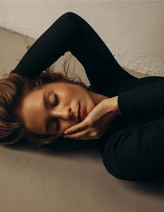 Woman with brown hair lying down in black turtleneck sweater against neutral background in contemplative pose - Hydrafacial in Evansville, IN