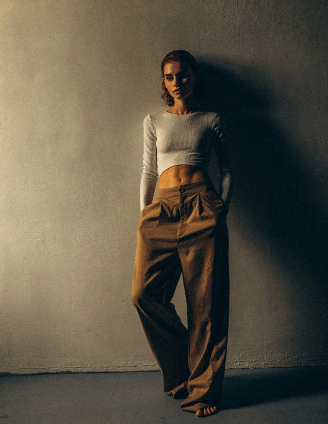 Woman in white crop top and brown wide-leg pants standing against minimalist wall in natural lighting - Weight management in Evansville, IN